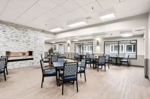 Bright and spacious dining area with modern decor, featuring tables and chairs arranged around a stone fireplace.