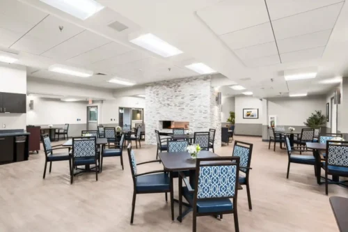 Bright and spacious dining area with modern decor, featuring tables and chairs arranged around a stone fireplace.