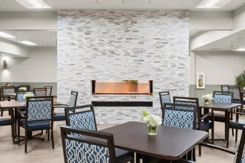 A modern dining area with dark wooden tables and chairs featuring blue patterned upholstery. A sleek, white stone wall with a decorative niche adds elegance.
